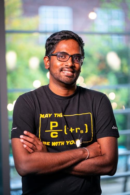 Men smiling with arms crossed across his chest in black Tshirt with yellow writing