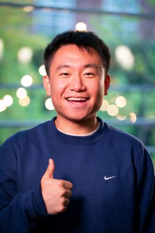 Man smiling in a Blue Nike sweater giving a thumbs up